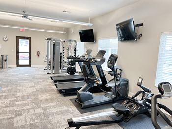 a gym with cardio equipment and a tv on the wall
